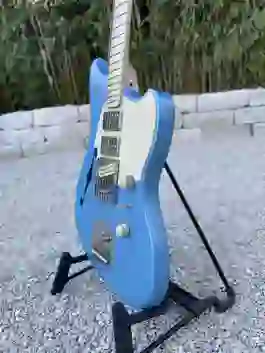 Eine handgefertigte blaue semiakustische E-Gitarre mit cremefarbenem Schlagbrett steht auf einem Gitarrenständer im Freien