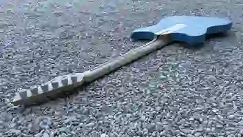 Rückansicht einer blauen E-Gitarre mit naturfarbenem Ahornhals auf Kies