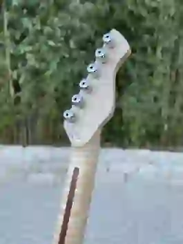 Nahaufnahme der naturfarbenen Kopfplatte einer blauen E-Gitarre mit sechs silbernen Mechaniken vor unscharfem Grün