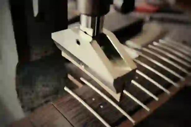 Beim Bundmontageprozess im Gitarrenbau drückt ein Metallwerkzeug auf die Bünde eines hölzernen Gitarrenhalses.